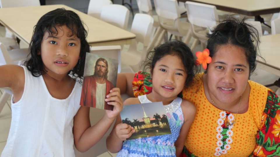 A-mother-and-her-two-daughters-from-New-Caledonia,-show-the-pictures-of-Jesus-Christ-and-the-temple-that-they-will-display-in-their-home.